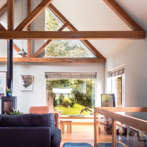 Interior of living room with exposed wooden roof struts, white walls, wood burning stove and dark blue sofa