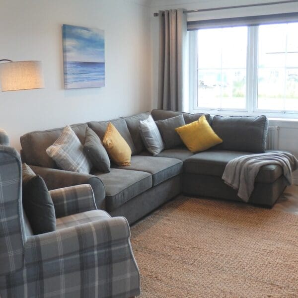 Lounge with white walls, grey couch and grey tartan wingback chair, Glen Brodie self catering, Dornoch