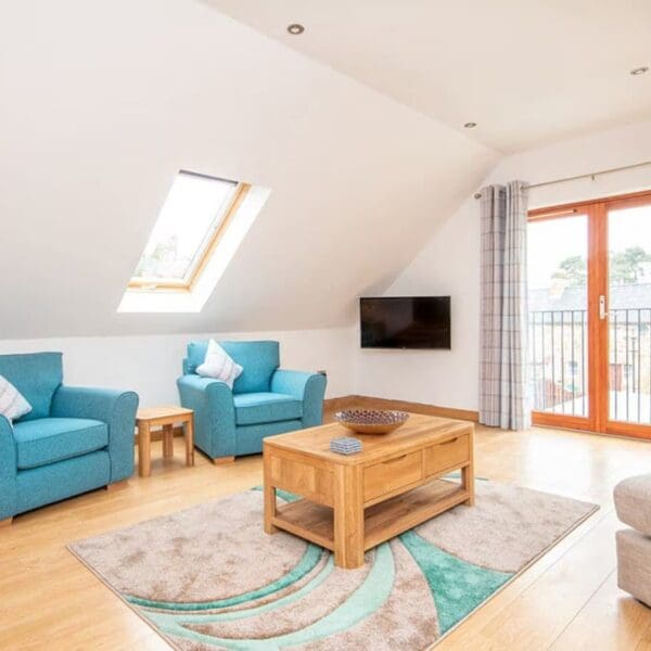Living area with two aqua blue armchairs and pine coffee table next to patio doors, The Hive holiday apartment, Dornoch
