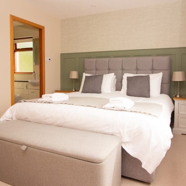 double bedroom in 18 The Meadows, Dornoch with grey headboard against a green and white wall, with door to ensuite and fabric storage box at foot of bed