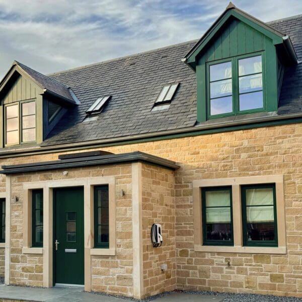 One and a half story house with sandstone walls, slate roof and green window surrounds