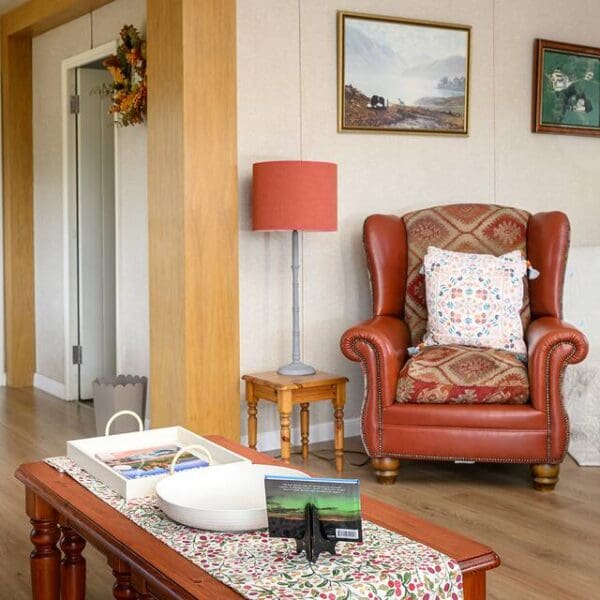 Living room area with wooden coffee table, brown leather wingback chair and coral coloured standard lamp