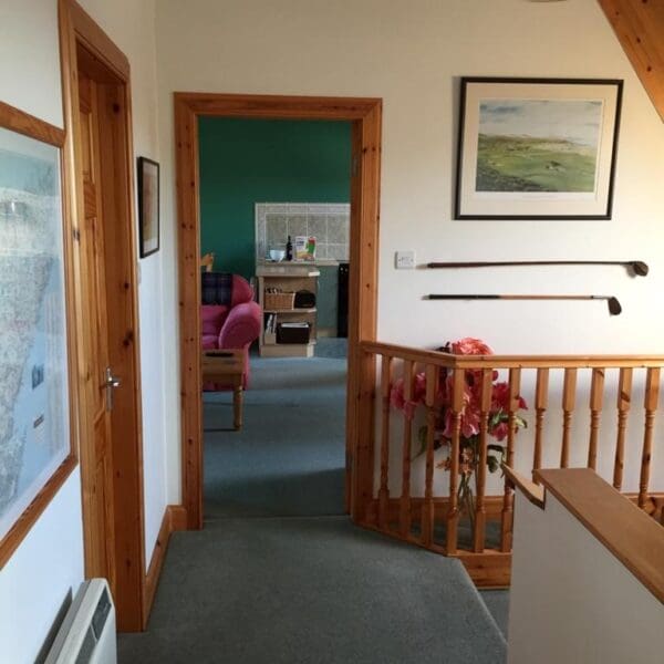 Upper stair landing with green carpet and pine bannister with golf clubs and pictures on the wall, West Dune apartment Dornoch