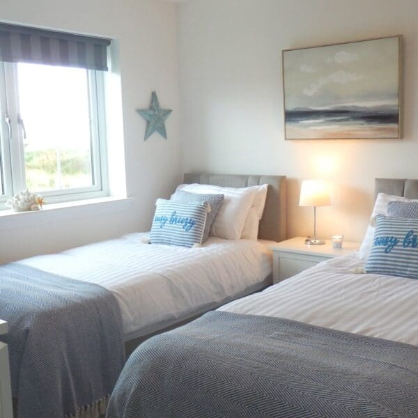 Twin bedroom with seaside theme, blue bedspreads and landscape painting on wall. Glen Brodie self catering, Dornoch