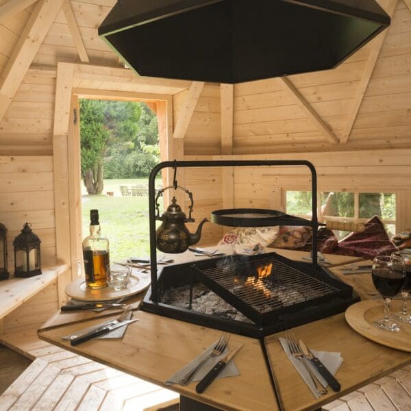 Interior of wooden barbecue hut with central table with fire pit in middle and large vent above