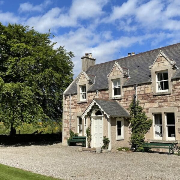 Exterior of Balloan House, Dornoch with trees and lawn on sunny day