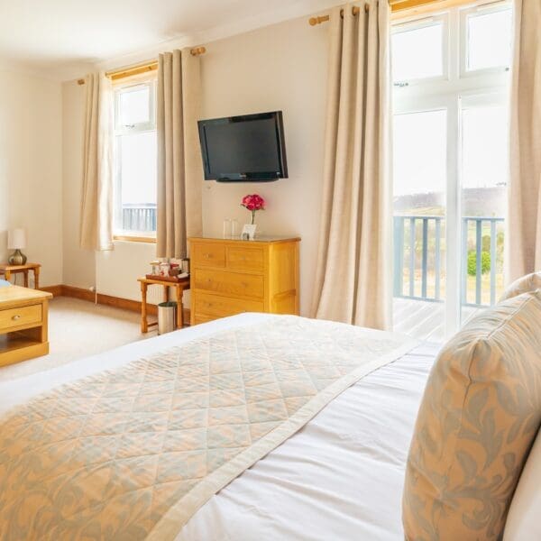 Double bedroom with patio doors, blue couch and tv on wall, Strathview Lodge B&B Dornoch