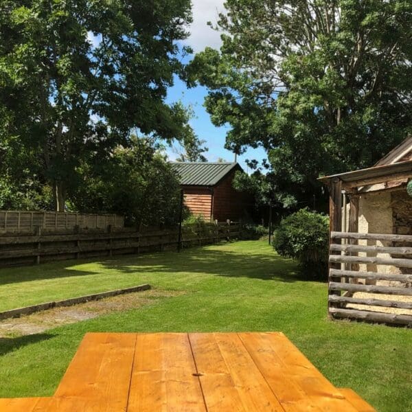 Rear garden of Carnegie Cottage, Dornoch with pine picnic table and grass lawn on sunny day