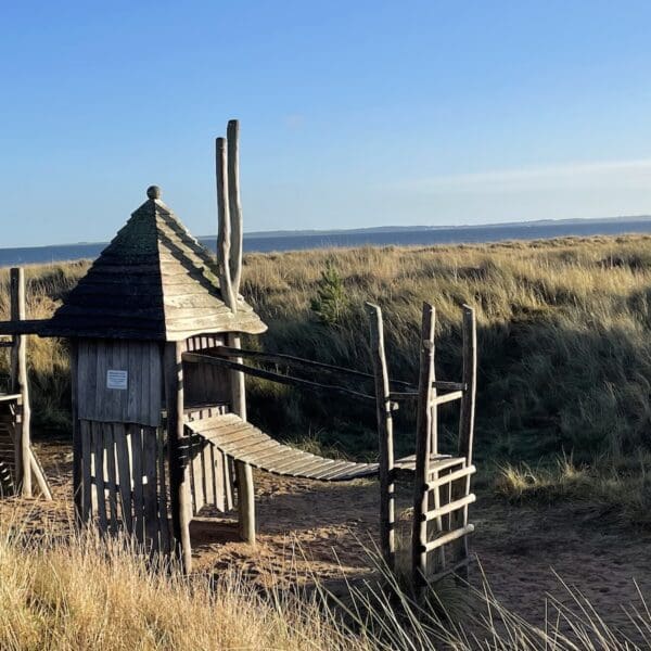 Children's play equipment in play park area set in sand dunes at beach with blue skies on sunny day