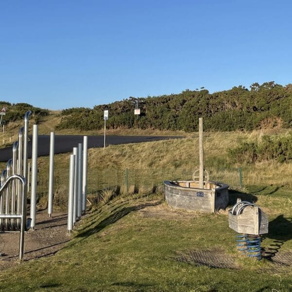 Children's play equipment in play park area set in sand dunes at beach with blue skies on sunny day
