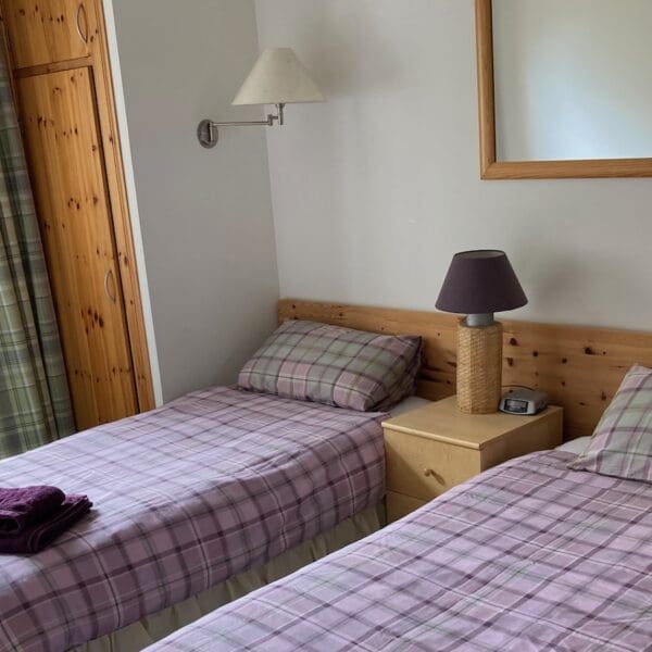 Twin bedroom with pine head board, pine wardrobe, purple tartan duvets and white walls in West Dune apartment, Dornoch