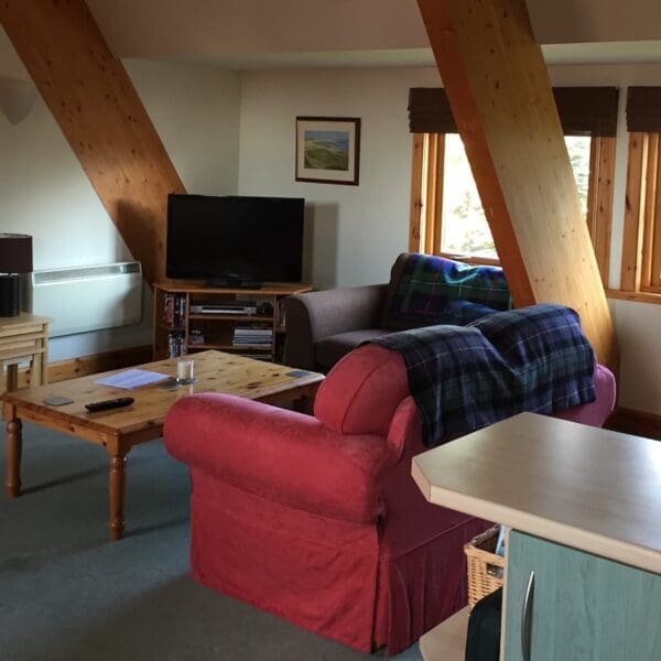 Open plan living room and kitchen area in West Dune apartment, Dornoch with pine features and red couches