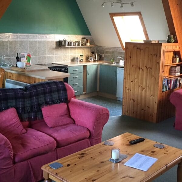 Open plan living room and kitchen with green and red decor in West Dune apartment, Dornoch