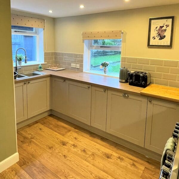 Kitchen with green painted wall, light wood counter top and grey kitchen units in Carnegie Cottage, Dornoch