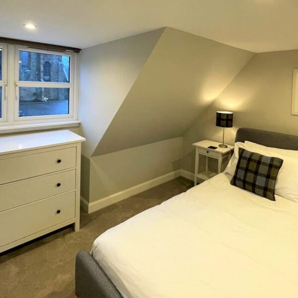 Double attic bedroom with grey decor and tartan cushions on white bedspread, Carnegie Cottage, Dornoch