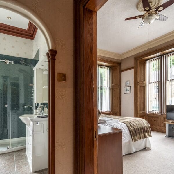 View into bedroom and bathroom from hallway with pitch pine door surrounds and cream walls, green shower tiles