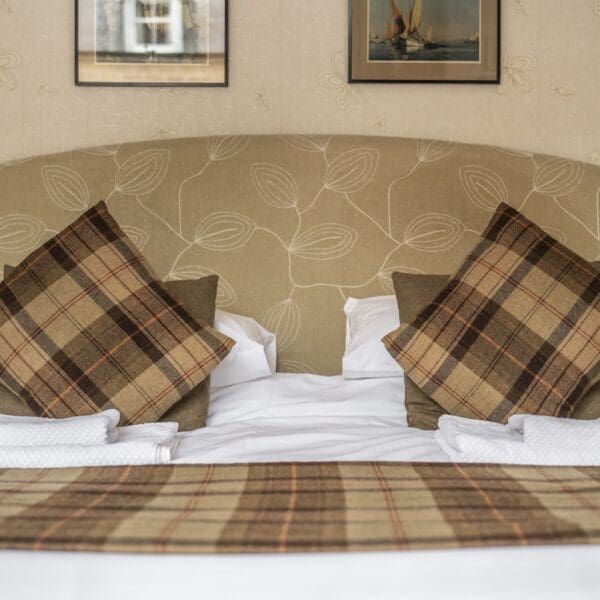 detail of bed with cream headboard, white sheets and brown tartan cushions and throw