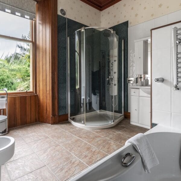 Bathroom with freestanding shower cabinet with green tiles, white toilet and bath, light brown floor tiles and pitch pine window surround