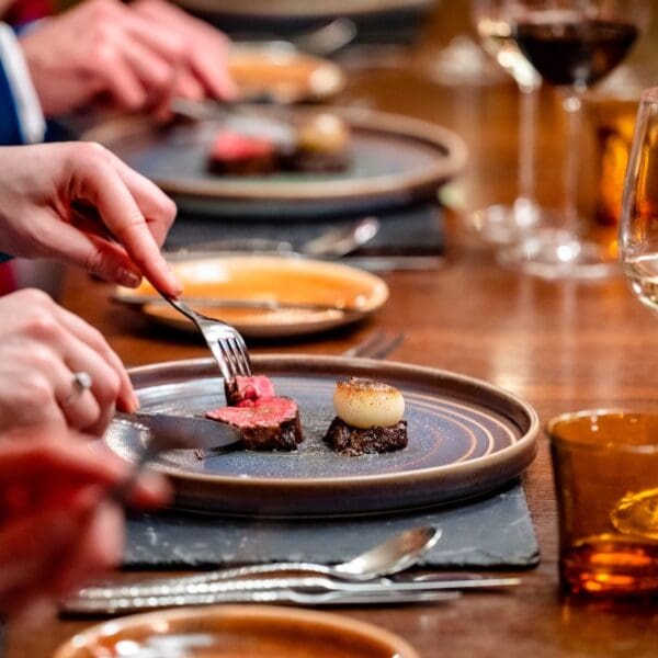 diners eating from dinner plates set on wooden dining table, glenmorangie house hotel