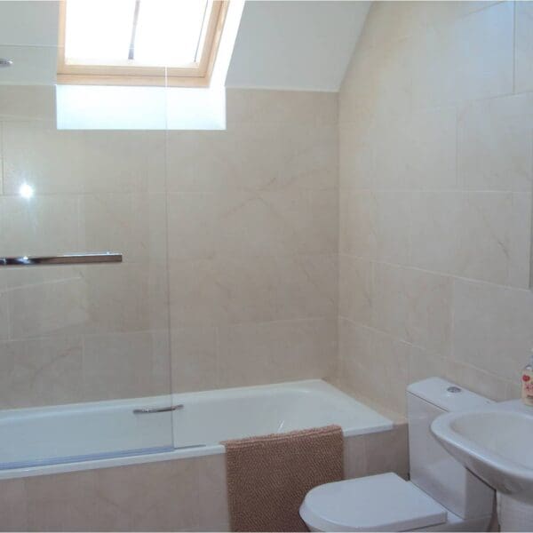 Bathroom with cream marble tiles and shower over bath in Frazier Cottage, Dornoch