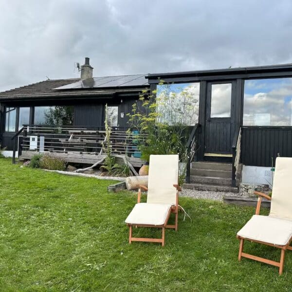 Sourth facing exterior of wooden cladded bungalow, with cream lawn chairs on grass, Wester Lonemore Dornoch