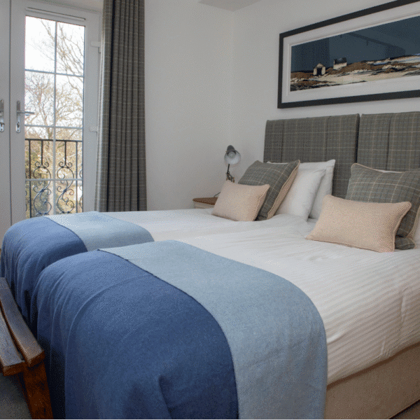 White bedroom with twin beds with white sheets and blue throw blankets. Grey headboards and a framed panoramic landscape painting on wall above