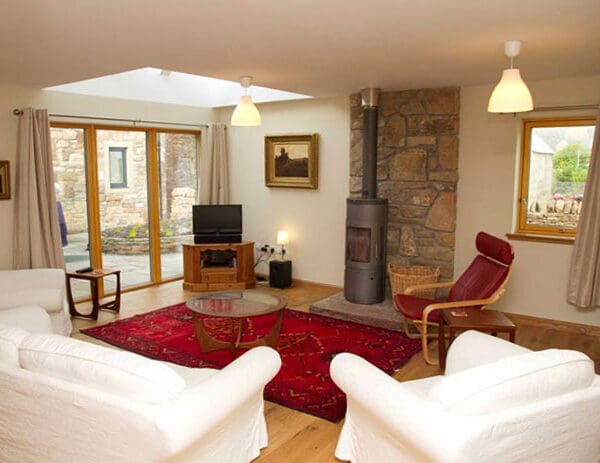Living room with red rug and wood burning stove in Frazier Cottage, Dornoch