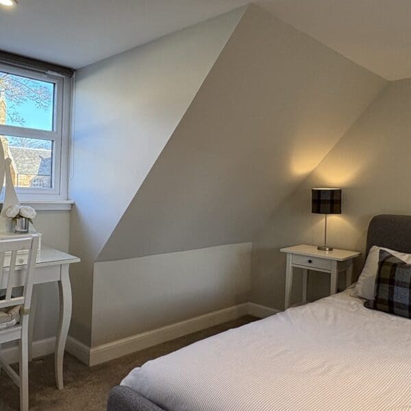 Double bedroom with grey walls, white bedspread and white dressing table below window