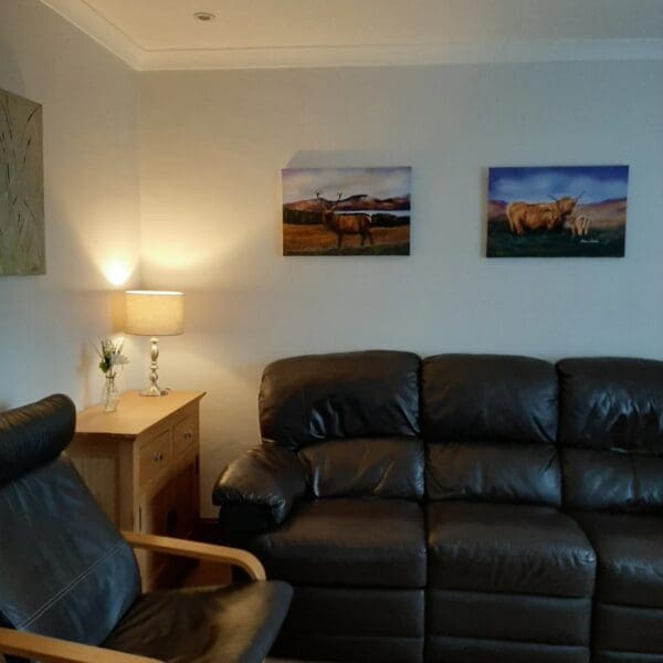 Living room with cream walls, dark brown leather suite and oak console table with lamp