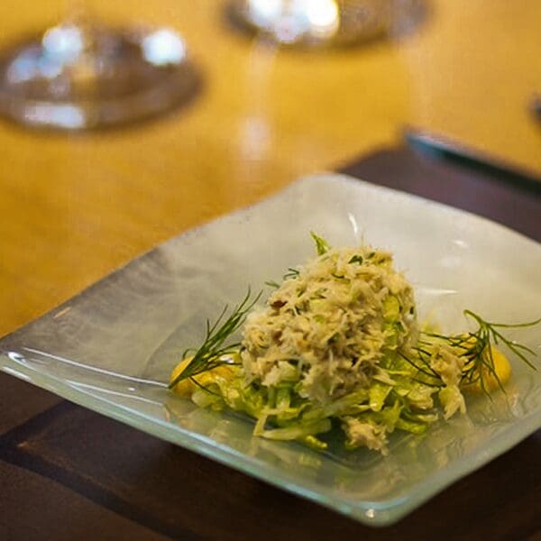 Crab salad starter on square white plate set on brown table mat