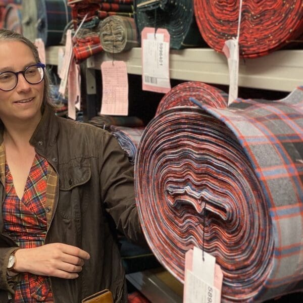 Female standing next to rolls of tartan bolts on shelves