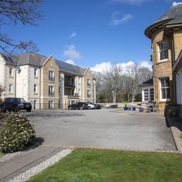 Apartment block with sandstone and white render exterior walls, car park in foreground