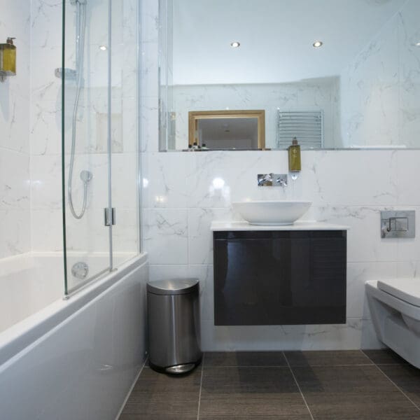 White marble bathroom with floating sink unit and shower over bath