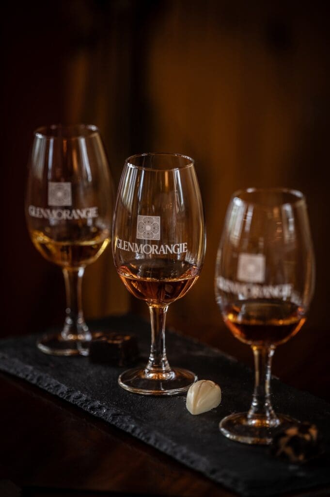 three whisky glasses engraved with Glenmorangie logo set on slate grey tray