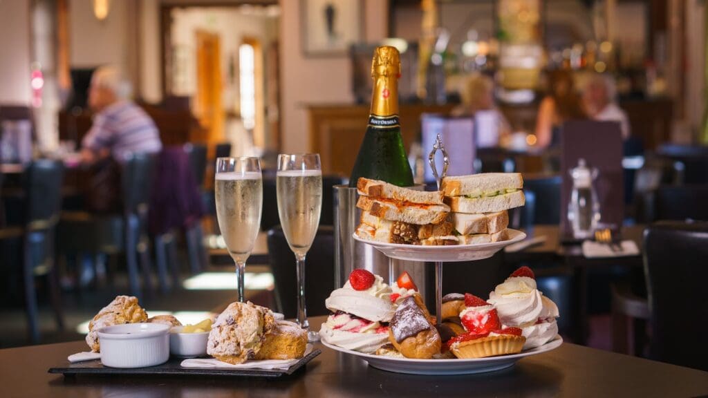 Afternoon tea sandwiches and cakes set on dark table in restaurant with two flutes of Champagne