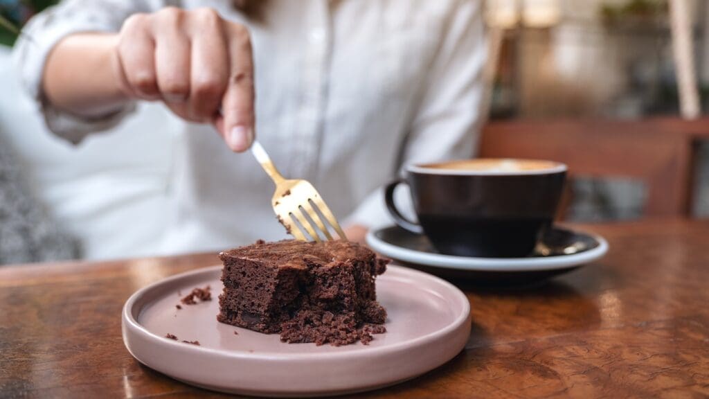 A woman cutting brownie cake with fork with coffee cup on wooden table in cafe