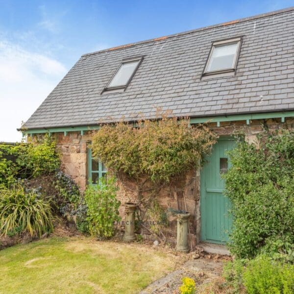 Exterior of stone cottage with slate roof. Green painted door and window frames. Climbing roses at door and green lawn in front