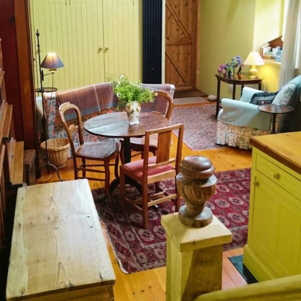 Cottage living room with cream walls and open plan kitchen lounge layout. Wooden dining table and chairs. Red rug on floor