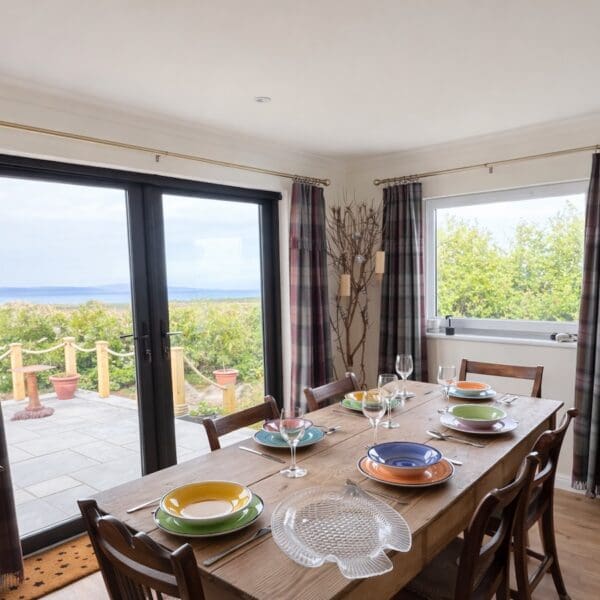Dining room with patio doors out to wooden decking area, wooden table set with colourful plates and bowls