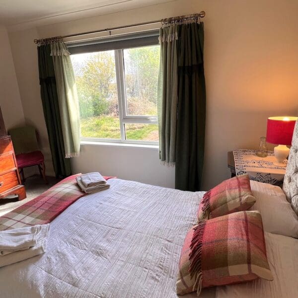 Double bedroom. Bed with white bedspread and red tartan rug and cushions. Large dark wood wardrobe, green curtains