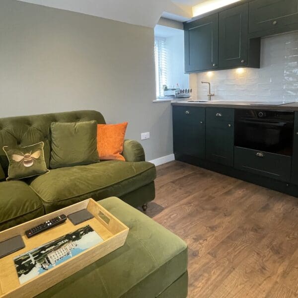 Cottage living room and kitchen, with black kitchen units, pale green painted walls and large squashy green couch with footstool