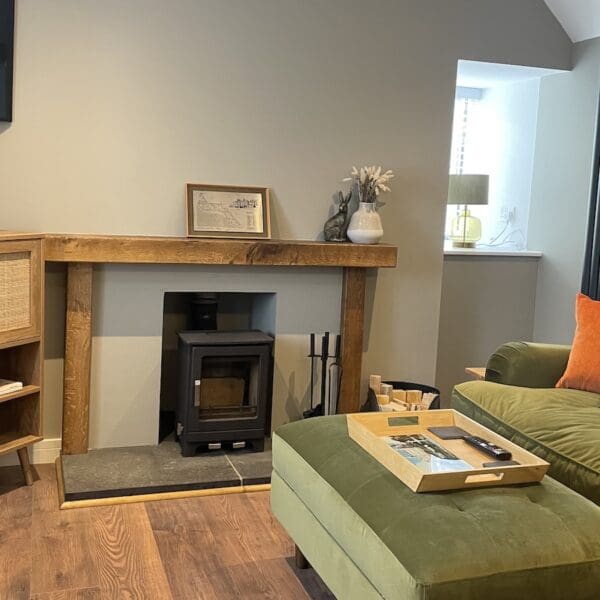 Cottage living room with cream walls, wood burning stove and large green couch with footstool