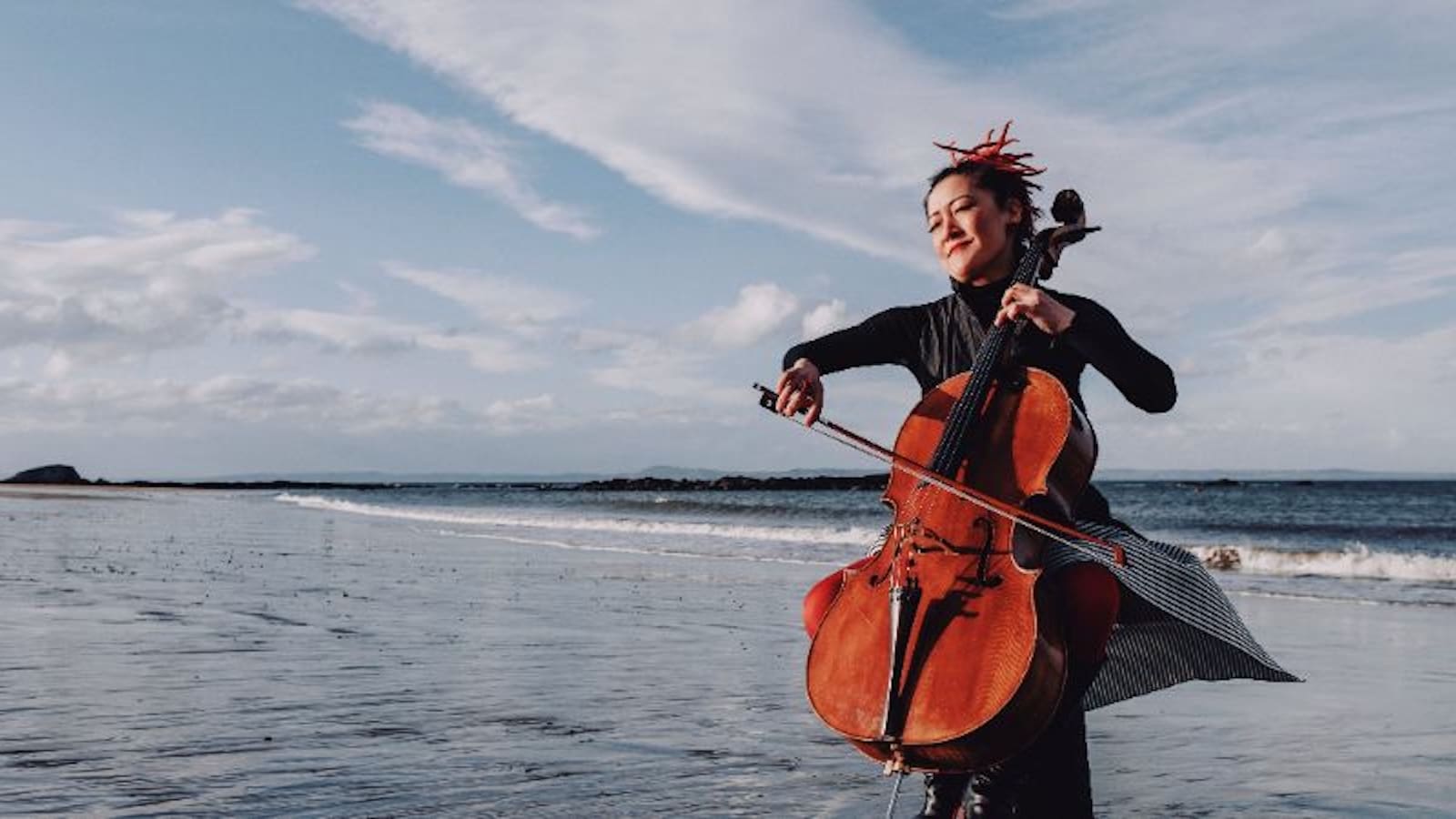 Woman playing cello on beach next to sea