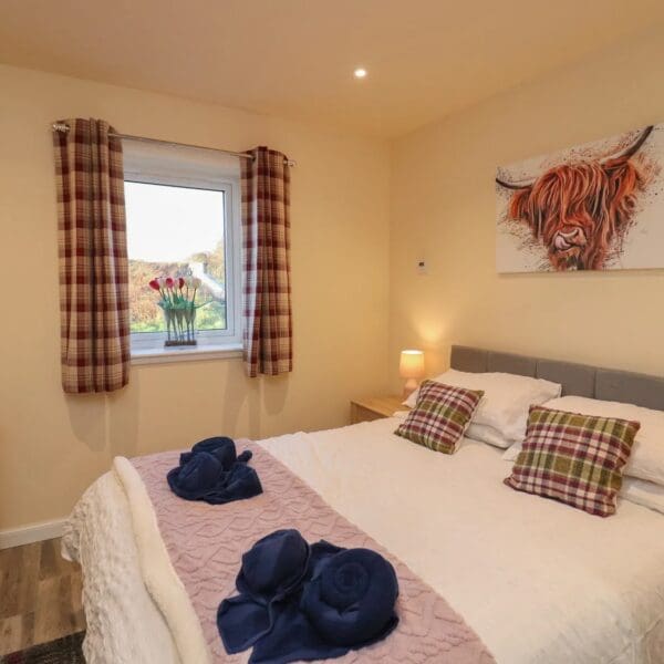 Double bedroom with cream walls, red tartan curtains and white bedspread with tartan cushions