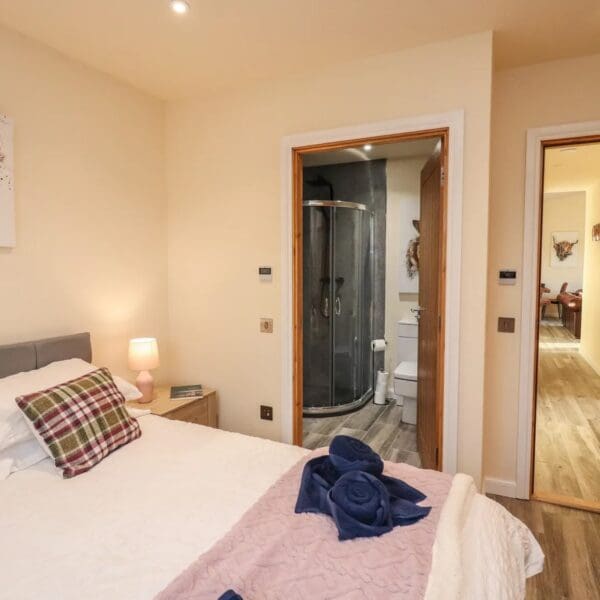 Double bedroom with cream wall and white bedspread, door leading to en suite shower room with black wet wall in shower cabinet