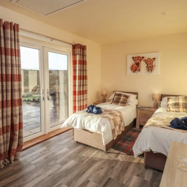 twin bedroom with two single beds with white bedspreads and red tartan cushions. Bedroom with cream walls and red tartan curtains