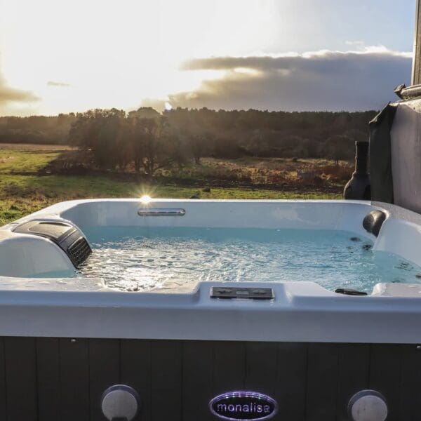 filled hot tub overlooking grass fields and woodland in evening setting sunlight