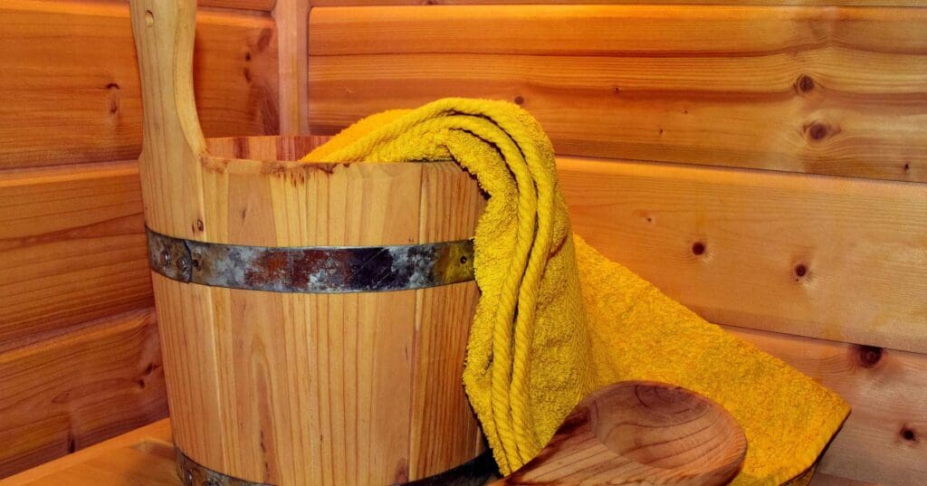 a photo in a sauna. There is a wooden bucket sat on a wooden bench with a handle coming out of it and a yellow towel.